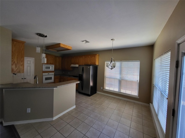 kitchen with visible vents, light tile patterned floors, a peninsula, white appliances, and a sink