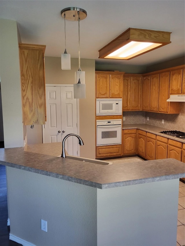 kitchen featuring under cabinet range hood, decorative backsplash, hanging light fixtures, white appliances, and a sink