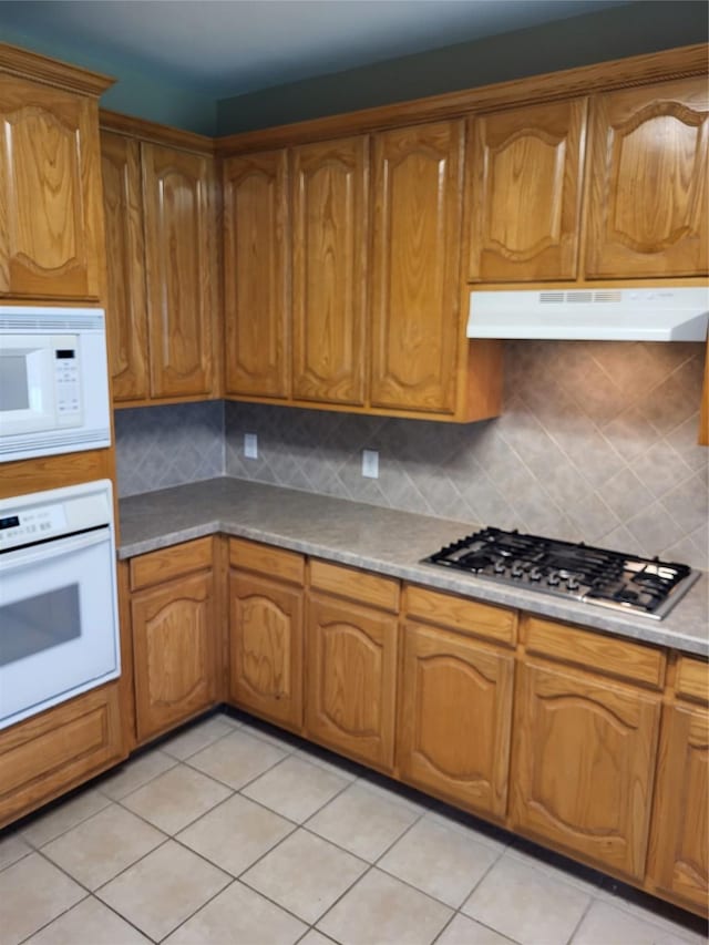 kitchen featuring under cabinet range hood, brown cabinets, and white appliances