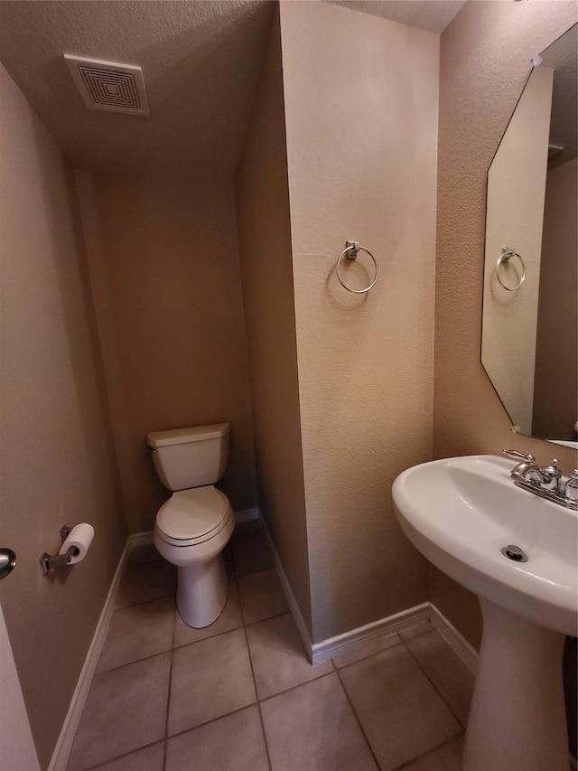 half bathroom with visible vents, baseboards, toilet, tile patterned floors, and a sink