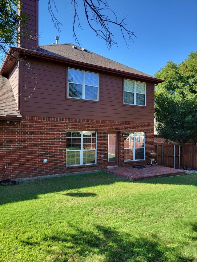 rear view of property with brick siding, fence, a chimney, a yard, and a patio