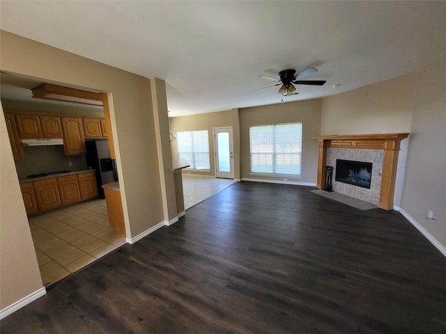 unfurnished living room featuring a tiled fireplace, baseboards, a ceiling fan, and wood finished floors