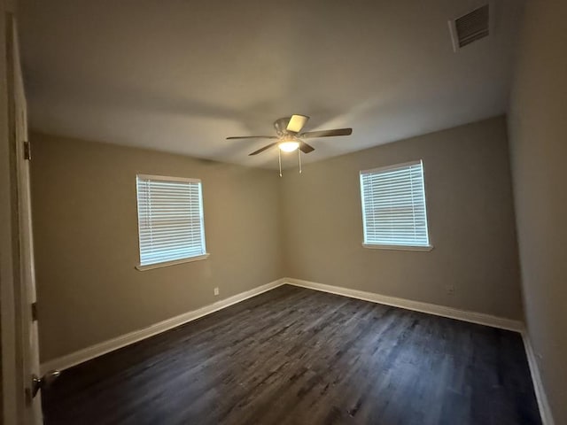 unfurnished room with visible vents, a ceiling fan, dark wood-type flooring, and baseboards