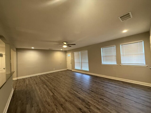 unfurnished room with ceiling fan, visible vents, baseboards, and dark wood finished floors