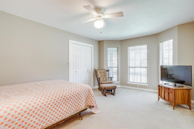 bedroom featuring light carpet, a ceiling fan, a textured ceiling, a closet, and baseboards