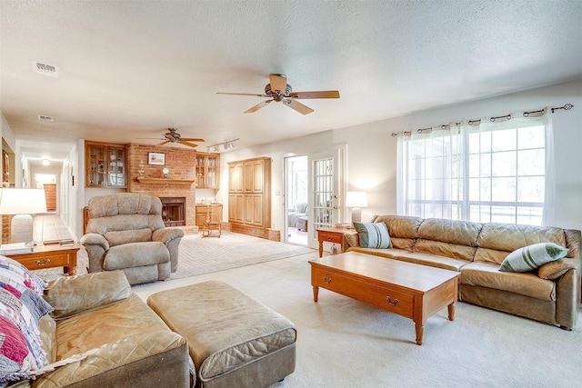 living room with visible vents, a textured ceiling, carpet floors, a fireplace, and ceiling fan