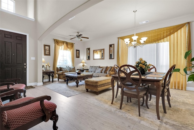 dining area featuring visible vents, baseboards, light wood-type flooring, ceiling fan with notable chandelier, and arched walkways