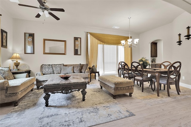 living area with visible vents, light wood finished floors, baseboards, arched walkways, and ceiling fan with notable chandelier