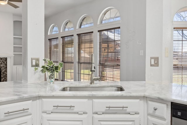 kitchen with light stone counters, white cabinets, ceiling fan, and a sink