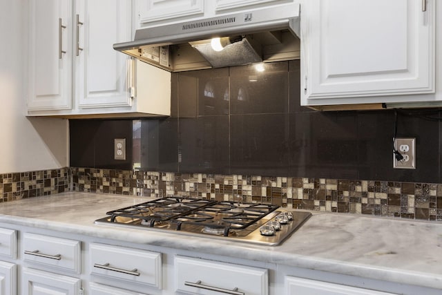 kitchen featuring under cabinet range hood, tasteful backsplash, white cabinetry, stainless steel gas stovetop, and light countertops