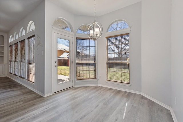 unfurnished dining area featuring baseboards, a notable chandelier, and wood finished floors