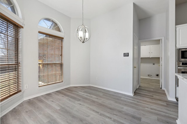 unfurnished dining area with light wood finished floors, a notable chandelier, and baseboards