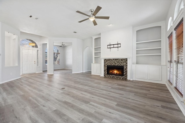 unfurnished living room featuring wood finished floors, a ceiling fan, visible vents, baseboards, and a tiled fireplace