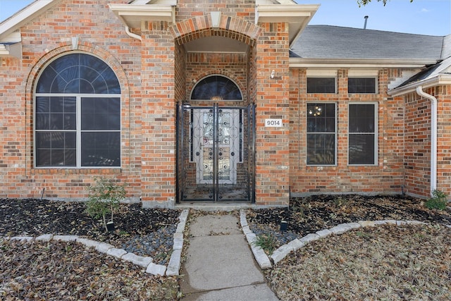 property entrance featuring french doors, brick siding, and a shingled roof