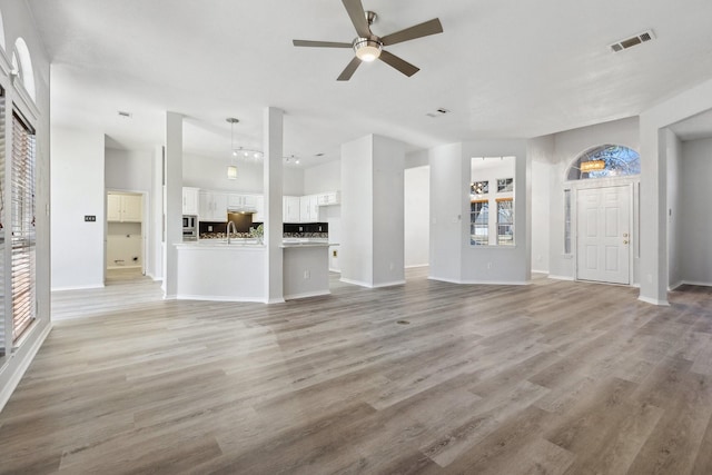 unfurnished living room featuring visible vents, a sink, light wood-style floors, baseboards, and ceiling fan