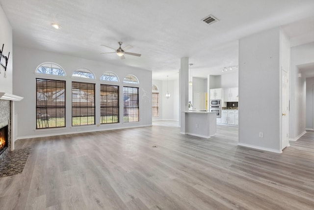 unfurnished living room with a tiled fireplace, visible vents, light wood-type flooring, and ceiling fan