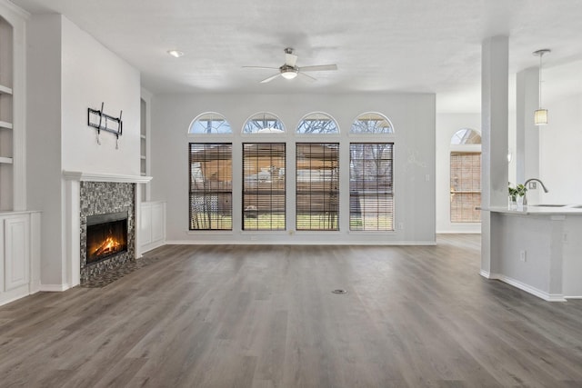 unfurnished living room with built in shelves, wood finished floors, baseboards, a fireplace with flush hearth, and a sink