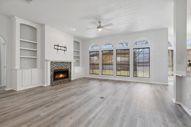 unfurnished living room with built in shelves, baseboards, a lit fireplace, and wood finished floors