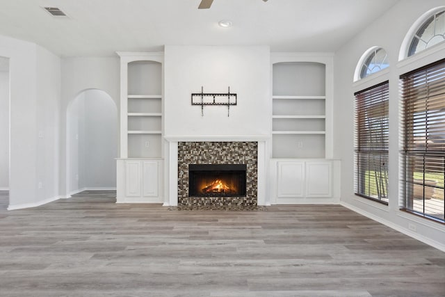 unfurnished living room featuring built in features, visible vents, baseboards, and wood finished floors