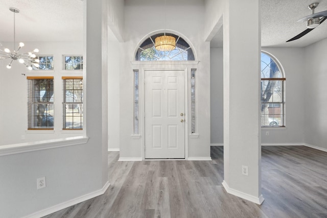 foyer featuring ceiling fan with notable chandelier, wood finished floors, baseboards, and a textured ceiling