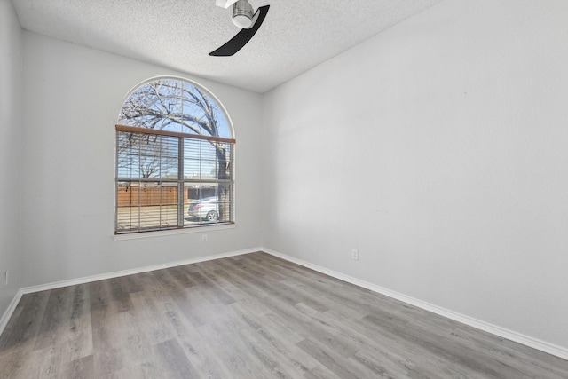 empty room with a ceiling fan, wood finished floors, baseboards, and a textured ceiling