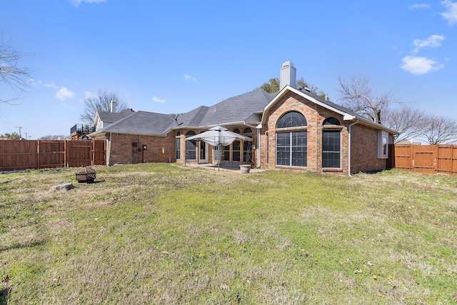 back of house featuring a lawn, a patio, a fenced backyard, brick siding, and a chimney