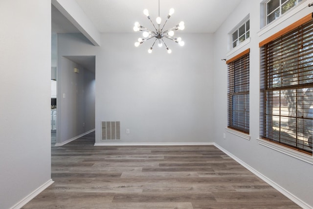 empty room with visible vents, baseboards, wood finished floors, and a chandelier