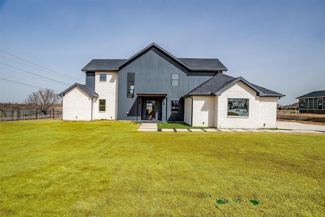 view of front of property with brick siding, board and batten siding, a front lawn, fence, and roof with shingles