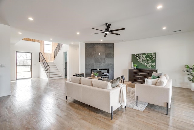 living room featuring recessed lighting, light wood-style flooring, stairs, and a tile fireplace