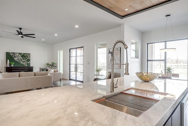 kitchen with recessed lighting, light stone countertops, open floor plan, and a sink