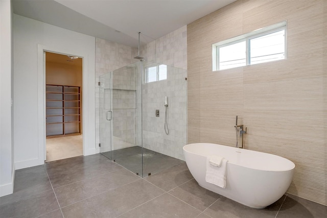 full bathroom featuring a soaking tub, a stall shower, tile patterned flooring, a spacious closet, and tile walls