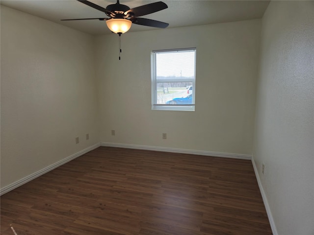 spare room featuring dark wood-type flooring, a ceiling fan, and baseboards