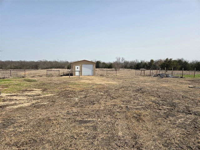 view of yard with a garage, a rural view, an outdoor structure, and fence