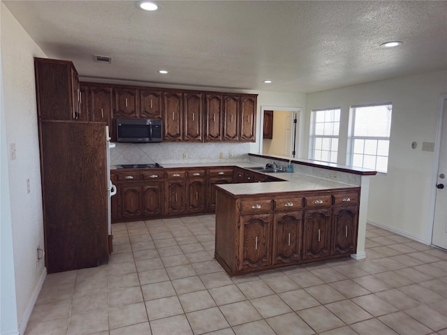 kitchen with visible vents, a peninsula, stainless steel microwave, black electric stovetop, and backsplash