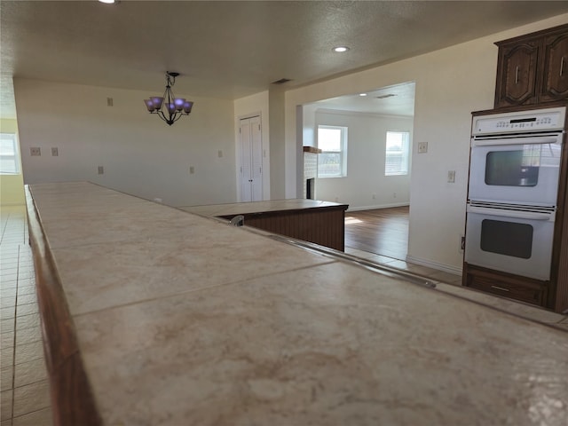 kitchen featuring baseboards, tile counters, dark brown cabinets, double oven, and a notable chandelier