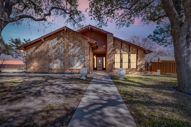 mid-century home featuring brick siding, stone siding, a front yard, and fence