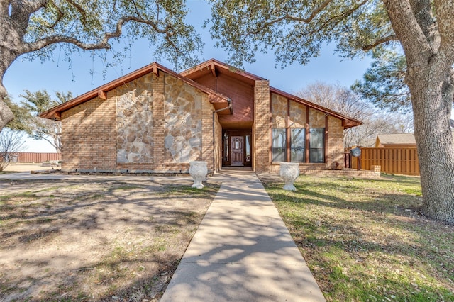 mid-century inspired home featuring a front yard, fence, brick siding, and stone siding