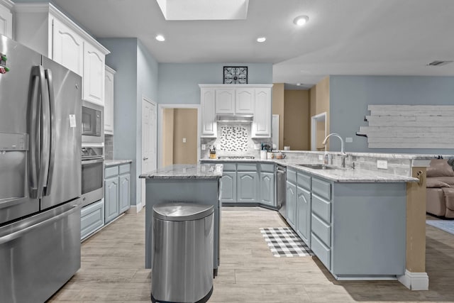 kitchen with a sink, tasteful backsplash, appliances with stainless steel finishes, a peninsula, and a skylight