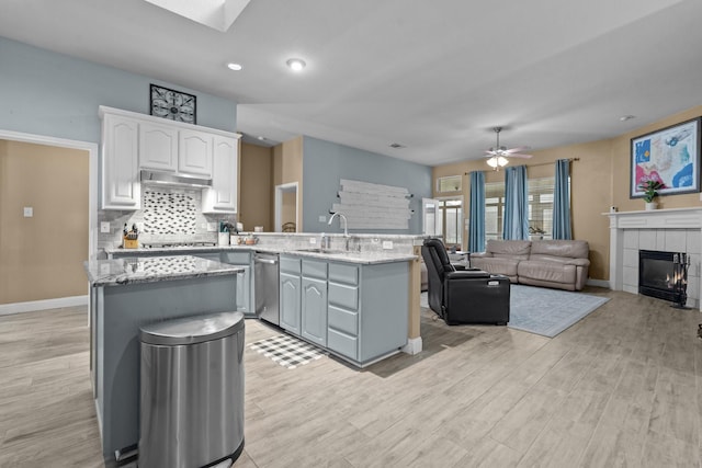 kitchen featuring under cabinet range hood, a tile fireplace, appliances with stainless steel finishes, a peninsula, and a sink