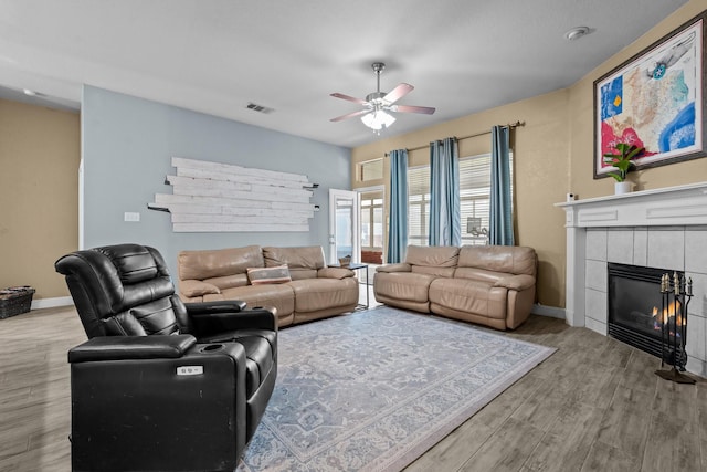 living room with visible vents, baseboards, ceiling fan, a tile fireplace, and wood finished floors