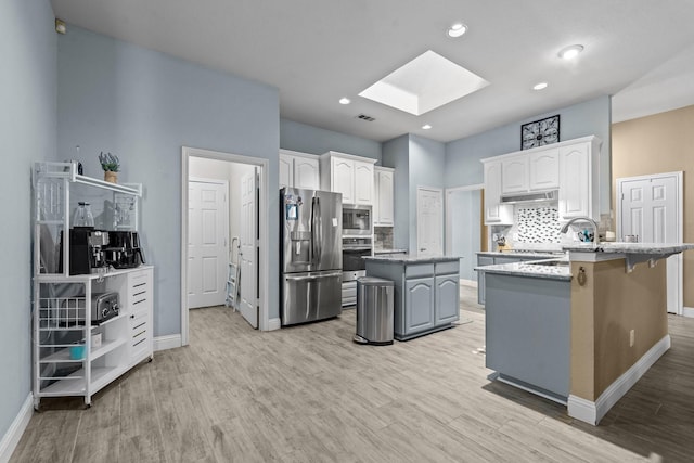 kitchen with a center island, decorative backsplash, a skylight, stainless steel appliances, and a sink