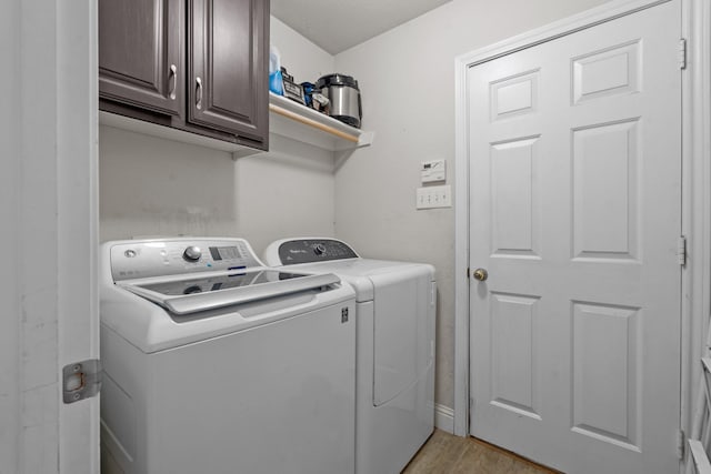 laundry room featuring light wood-style flooring, cabinet space, and washing machine and dryer