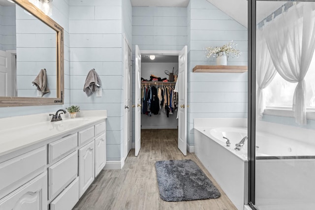 full bathroom with a walk in closet, wood finished floors, wooden walls, a bath, and vanity