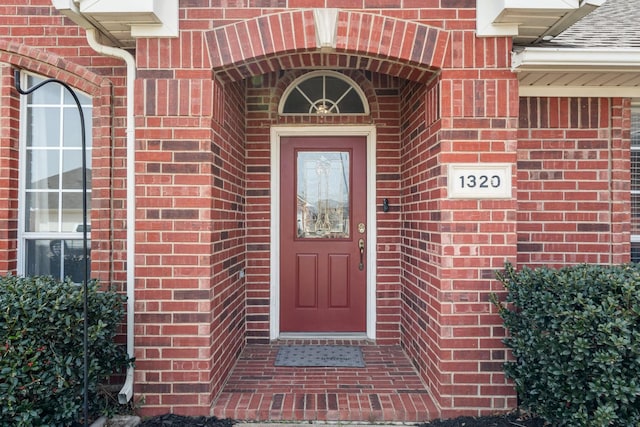 entrance to property featuring brick siding and roof with shingles