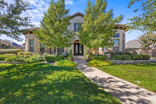 view of front of property featuring a front yard, fence, stone siding, and french doors