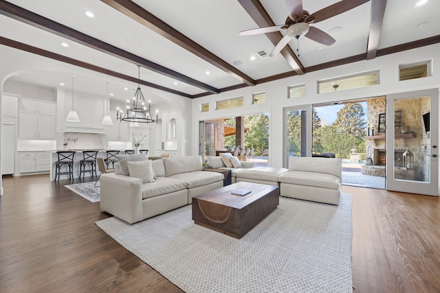 living room with beamed ceiling, arched walkways, a warm lit fireplace, and dark wood finished floors