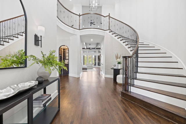 foyer featuring wood finished floors, baseboards, arched walkways, stairs, and a towering ceiling