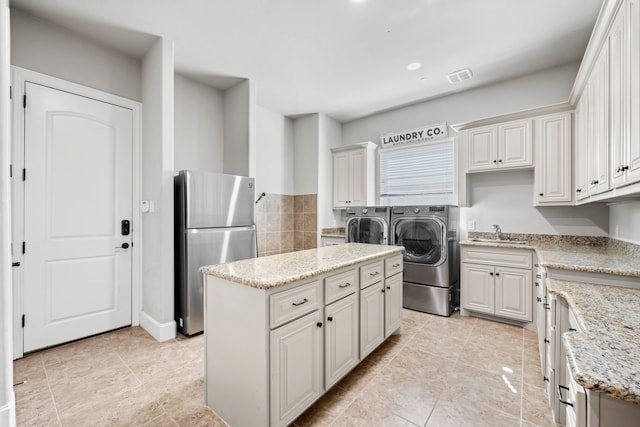 kitchen featuring visible vents, a kitchen island, freestanding refrigerator, a sink, and washer and clothes dryer