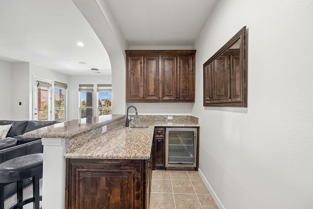 bar with a sink, wine cooler, arched walkways, light tile patterned floors, and baseboards