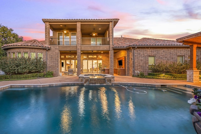 back of property with a pool with connected hot tub, a tile roof, a balcony, a patio area, and a ceiling fan